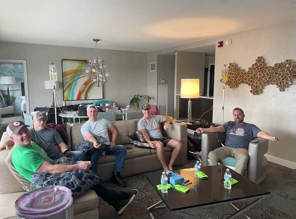 Nashville IV FluidsFive men sitting on couches in a living room setting, receiving IV hydration therapy, with IV bags visible in the background - Nashville IV Fluids Nashville IV FluidsFive men sitting on couches in a living room setting, receiving IV hydration therapy, with IV bags visible in the background - Nashville IV Fluids